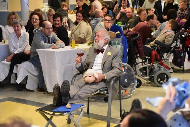 Alfred Marmann auf einem Ehrenplatz inmitten seiner Gäste und Geschenken, hebt fröhlich ein Weinglas.