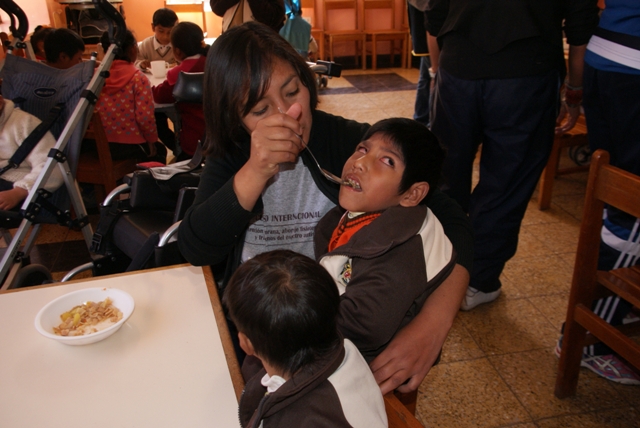 Die Mensa der Schule in Cusco. Ein Kind bekommt Hilfe beim Essen.